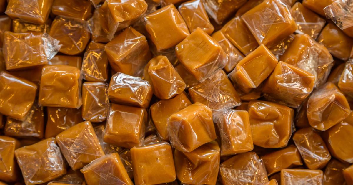 Close-up of a large pile of caramel candies. Each of the pieces of candy features clear plastic wrapping.
