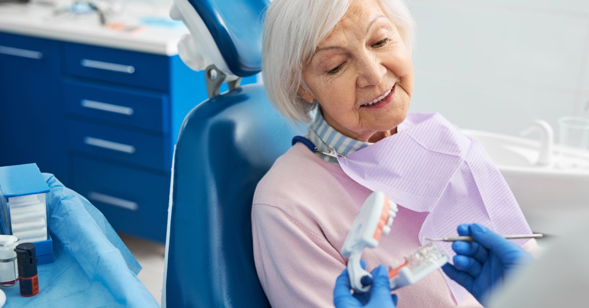 An older female dentist patient is looking at a dental model demonstrated by a dentist's blue gloved hands.