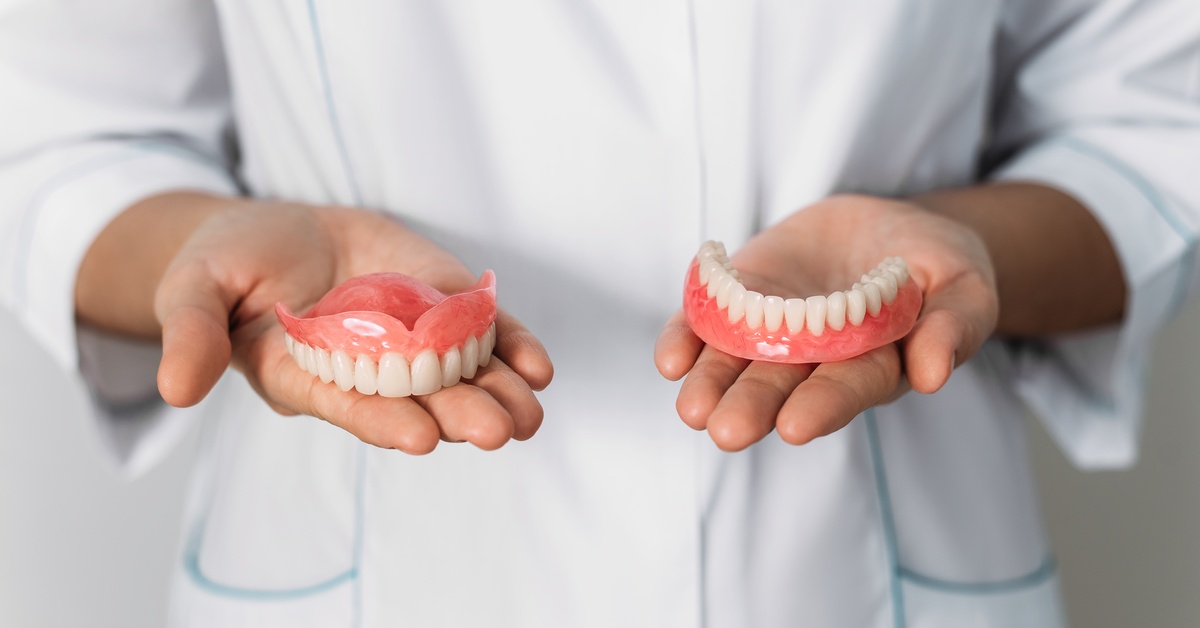 A person in a white lab coat holds the top and bottom pieces of a set of dentures in their open palms.