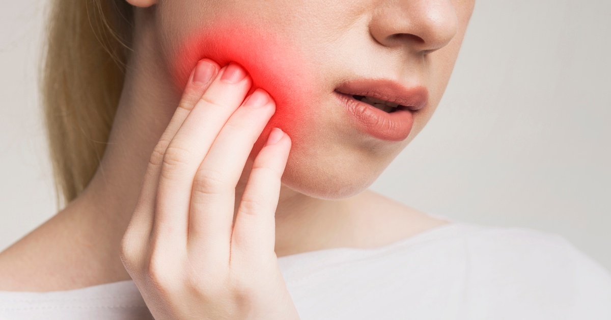 A close-up of a person pressing their hand to their cheek with a red highlight over their jaw. Their lips are slightly parted.
