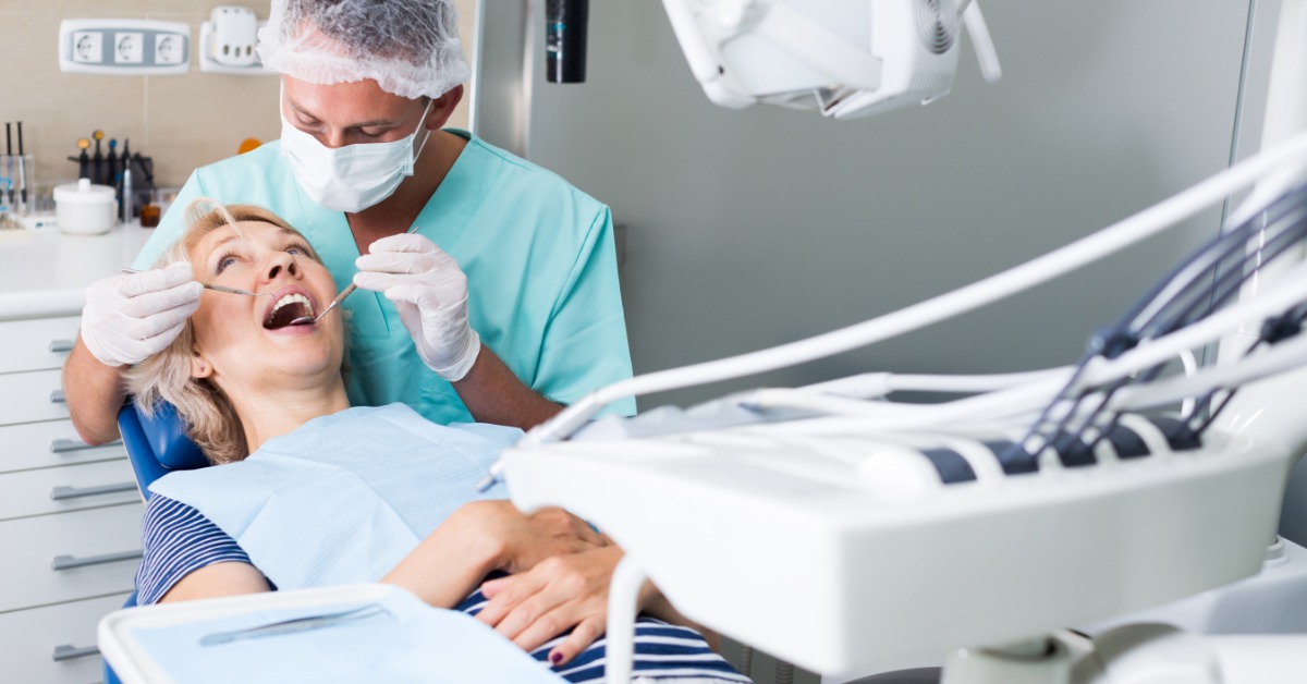 A dentist examines a woman’s teeth during a dental appointment while she reclines in a treatment chair.