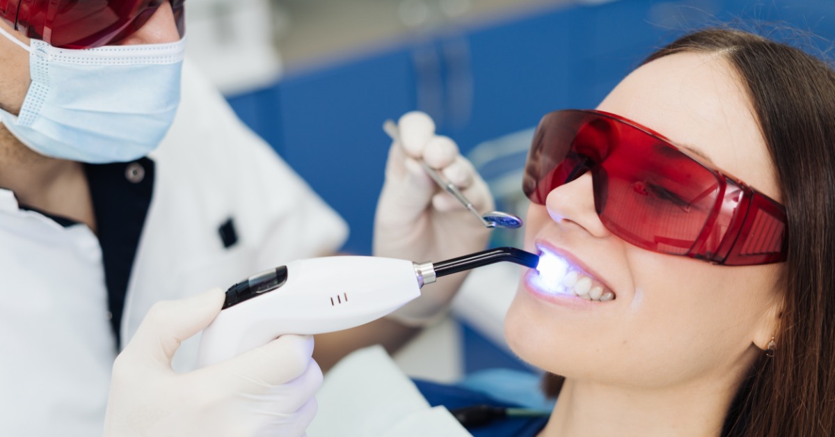 Patient wearing protective glasses receives a professional teeth whitening treatment while a dentist uses a curing light.