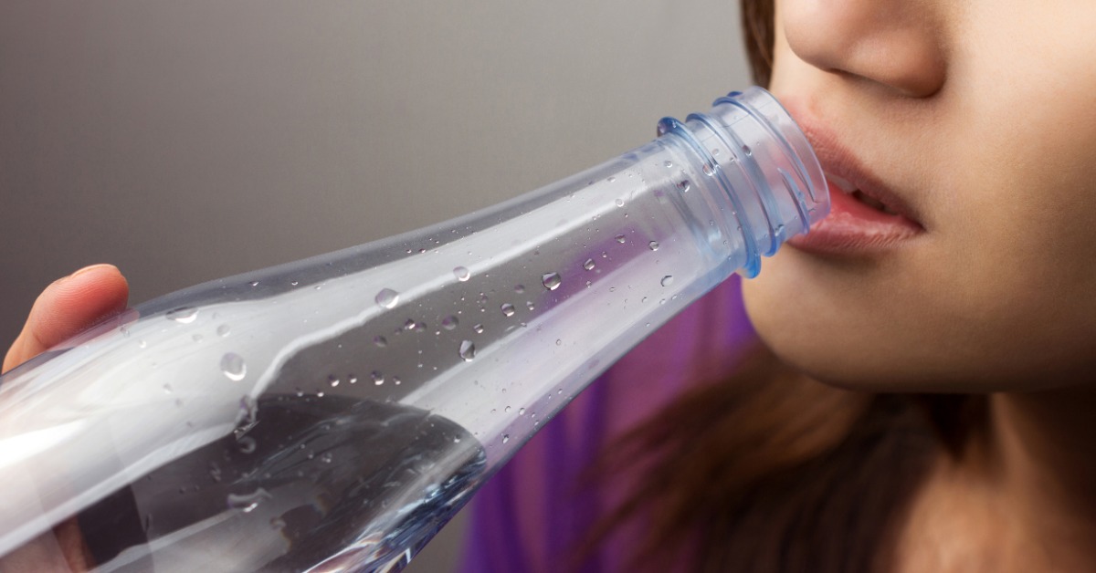 Woman drinking water from a clear plastic bottle, highlighting hydration as a way to help relieve dry mouth symptoms.