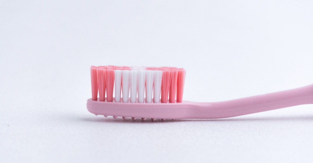 A pink manual toothbrush with pink and white bristles lying horizontally on a clean white background.